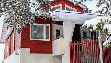 Uma casa vermelha de dois andares com varanda, número de porta visível e escadaria que leva ao segundo andar.