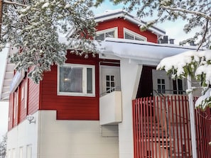 A red two-story house with a balcony, a visible door number, and a staircase leading to the second floor.