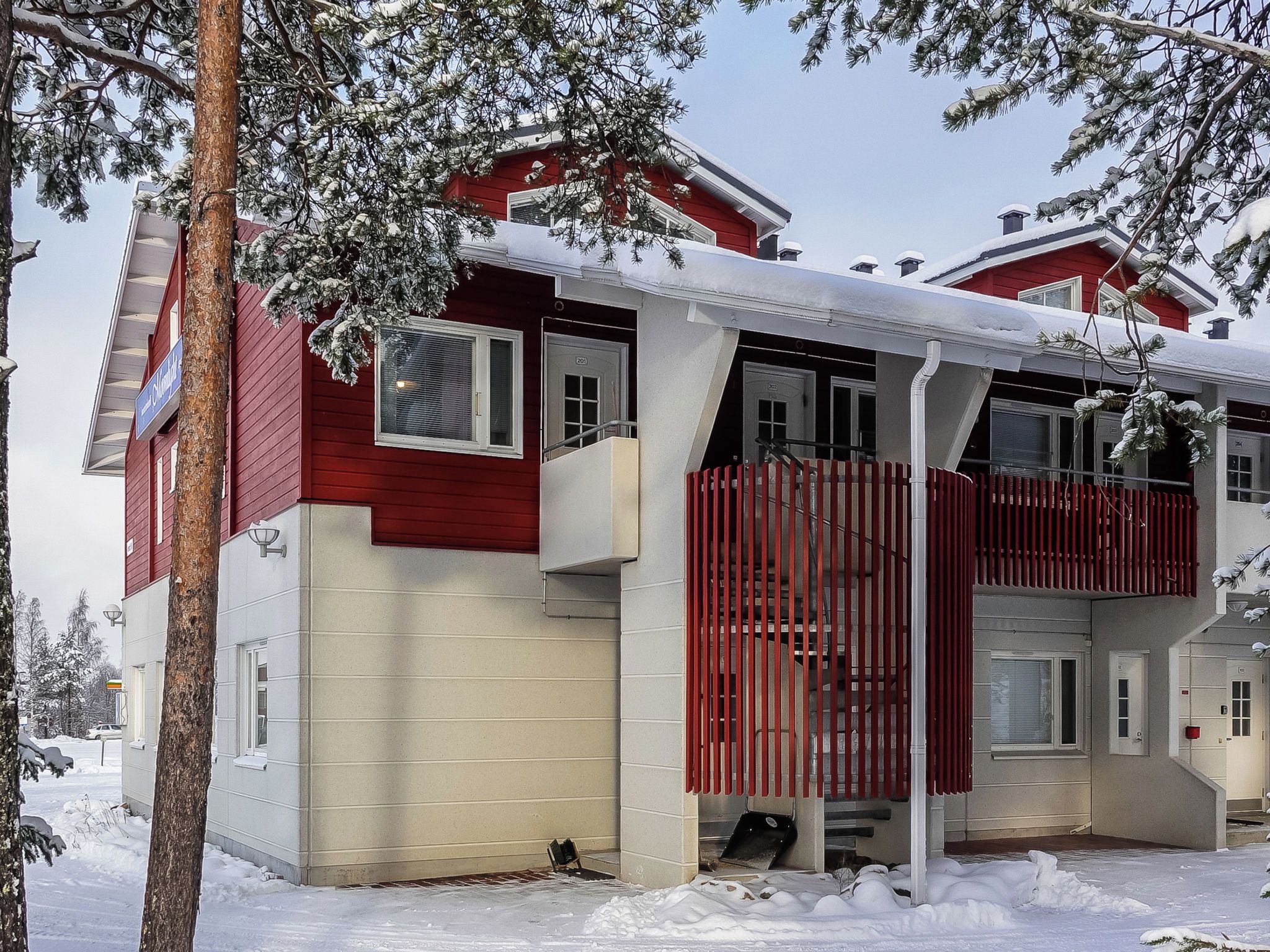 A two-story house with a red exterior and white trim, featuring a balcony and a covered porch area.
