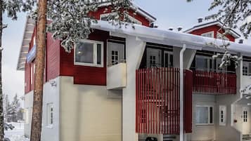 A two-story house with a red exterior and white trim, featuring a balcony and a covered porch area.
