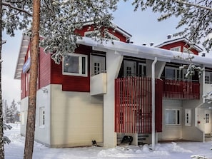 Punaisella maalilla maalattu, valkoisilla koristeilla varustettu kaksikerroksinen talo, jossa on parveke ja katettu kuisti.