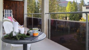 A balcony with a table set for two, featuring a chair, a small table, a candle, and a mug.