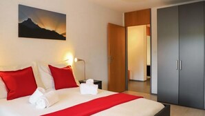 A modern hotel room with a large bed, red and white bedding, a bedside lamp, and a painting of a mountain on the wall.