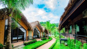 A pathway flanked by thatched-roof buildings with outdoor seating areas and lush greenery. - May Tropicall Villas (Hanoi)