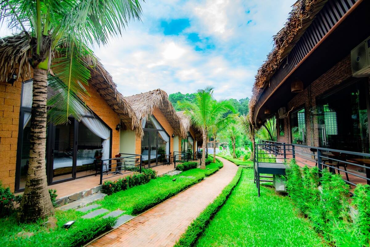 A pathway flanked by thatched-roof buildings with outdoor seating areas and lush greenery.
