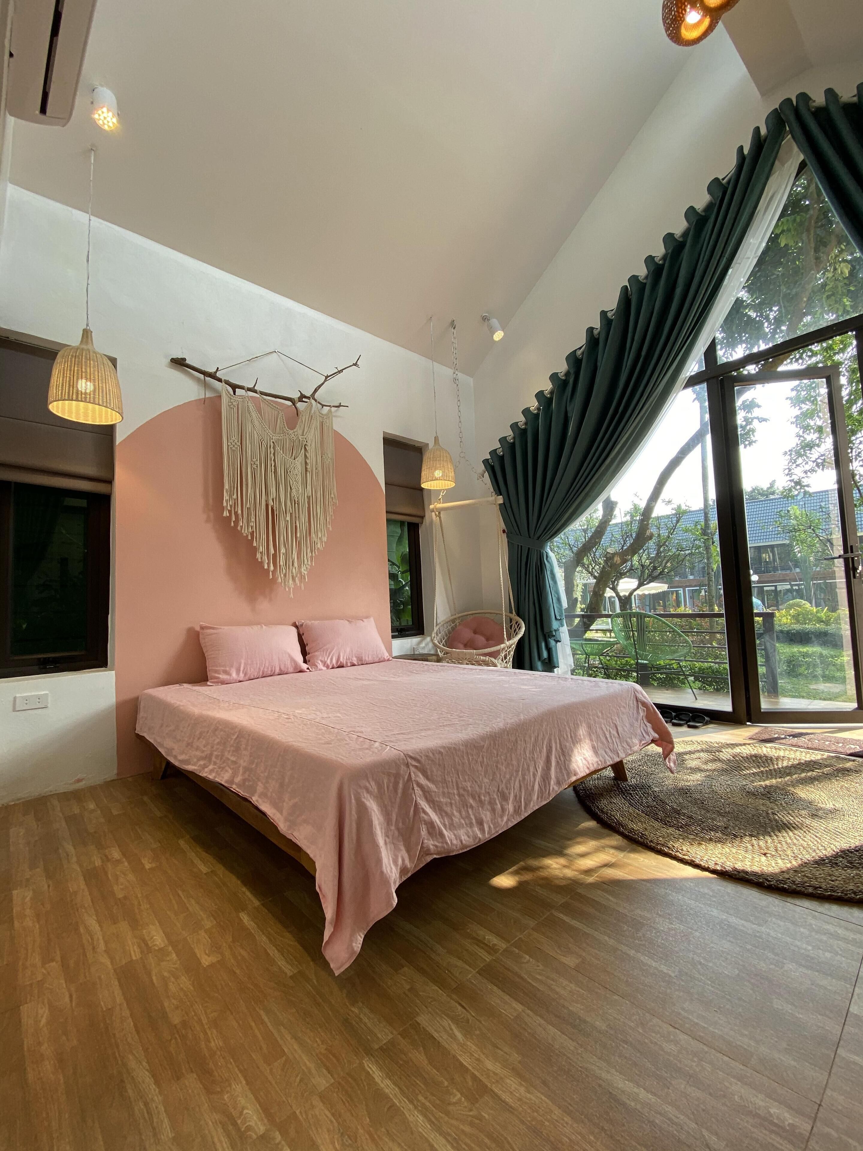 A bedroom with a large bed, a hanging macrame decoration, and a view of the outdoors through a large window.