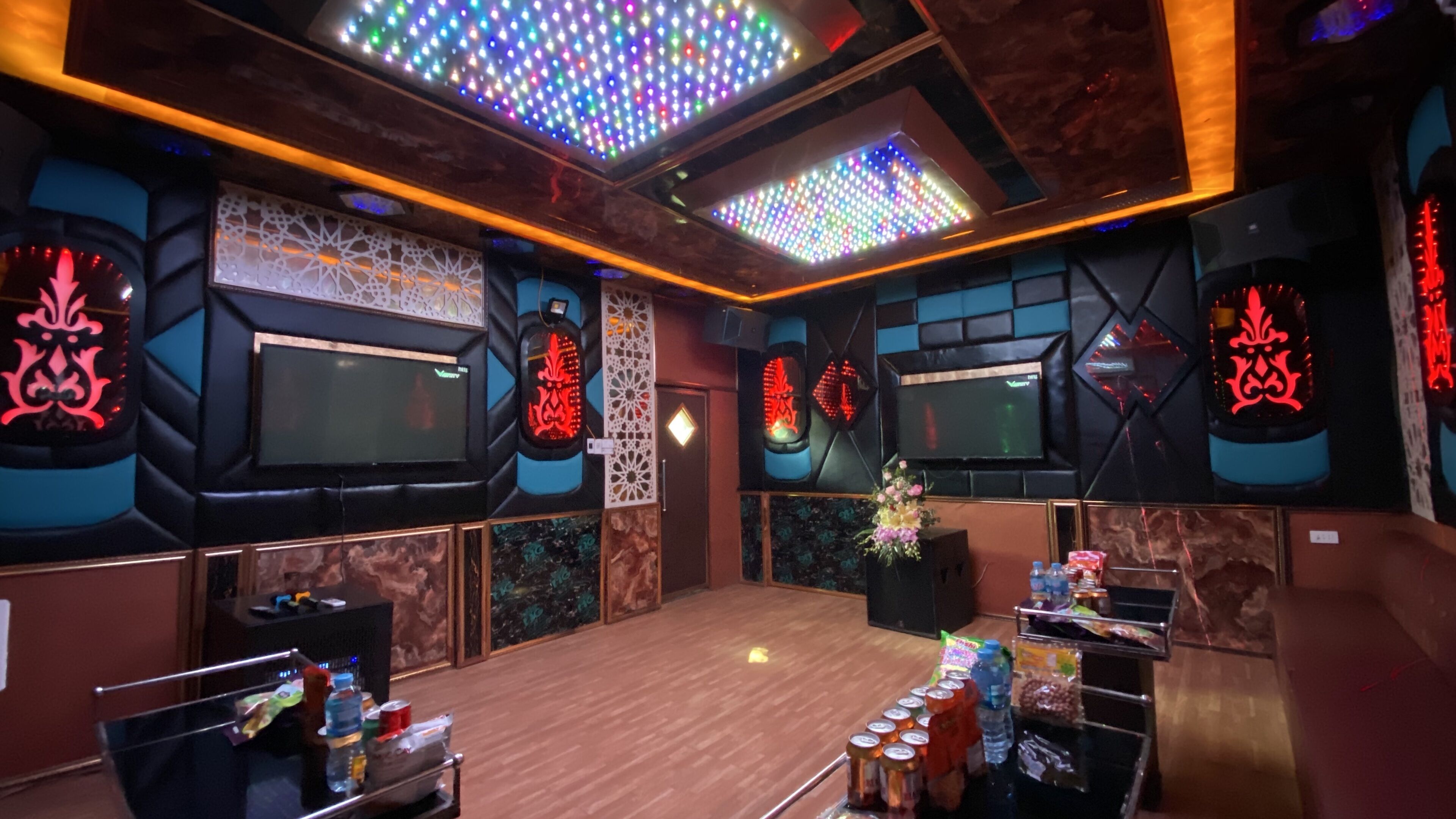 A room with a wooden floor, a stage with a speaker, and a table with snacks.
