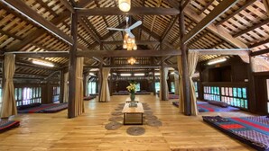 A spacious hall with a high wooden ceiling, a central table with a vase, and patterned mats on the floor. - May Tropicall Villas (Hanoi)
