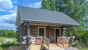 A log cabin with a porch, two doors, and a gravel driveway.