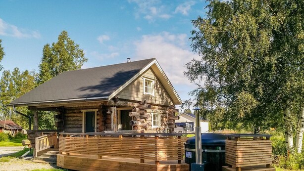 A log cabin with a stone foundation, wooden deck, and a covered outdoor area.