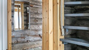 A wooden log cabin interior with a metal staircase and a mirror reflecting a window.