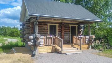 A log cabin with a porch and two doors, surrounded by trees.