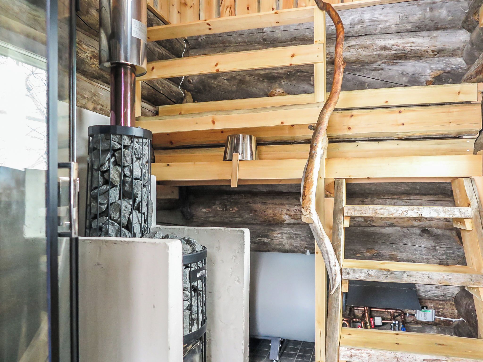 Ein Holzinnenraum mit Kamin aus Stein, einem Metallofen und einer Holztreppe.