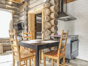 Uma cozinha rústica com parede de pedra, cadeiras de madeira, uma mesa de jantar, televisão e um forno moderno.