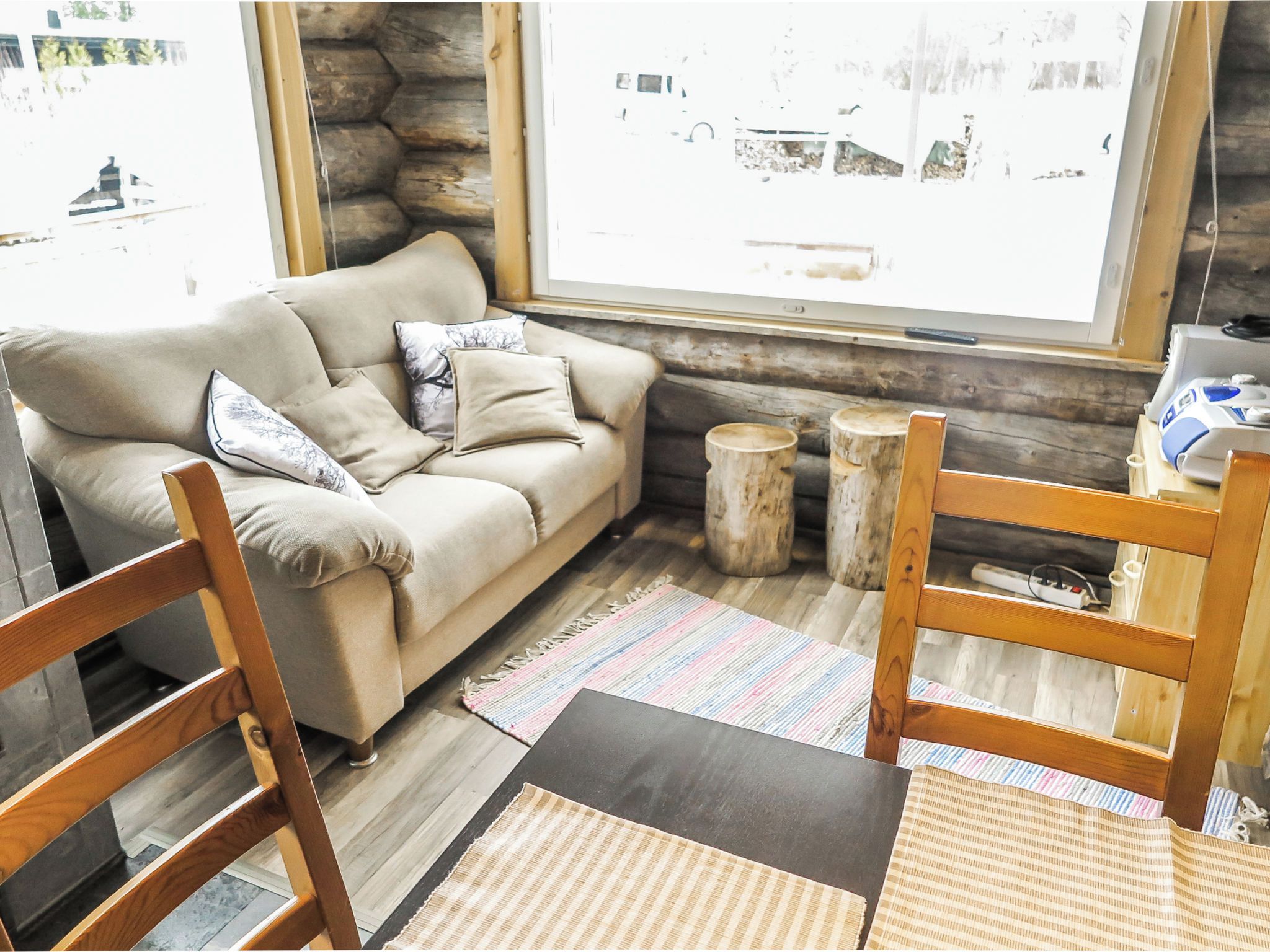 A cozy living room with a sofa, wooden chairs, a coffee table, and a large window with a view of the outside.