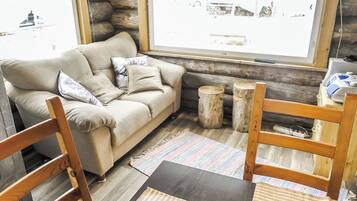A cozy living room with a sofa, wooden chairs, a coffee table, and a large window with a view of the outside.