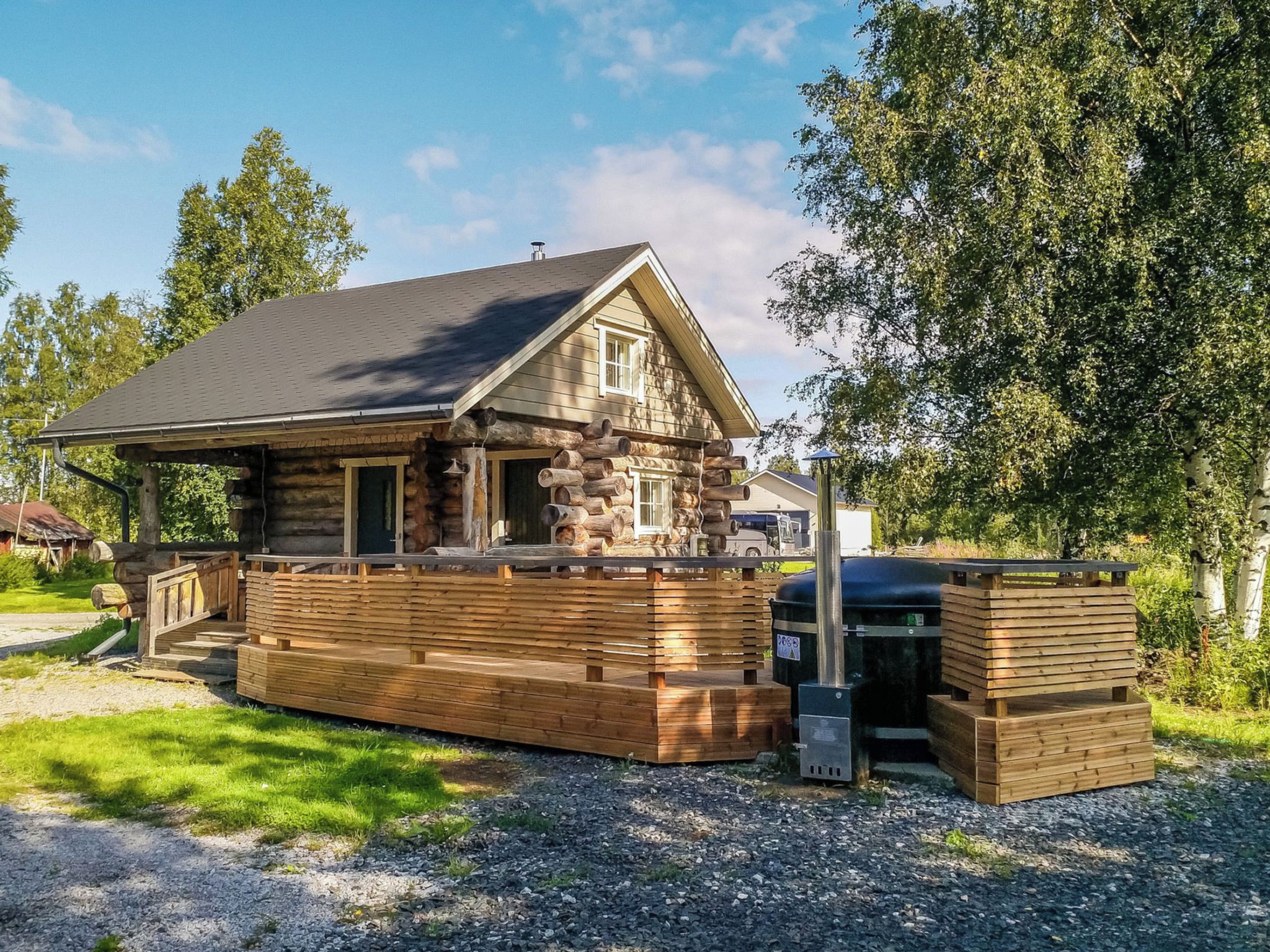 Eine Blockhütte mit Steinunterbau, einer Terrasse und einem Grillbereich.
