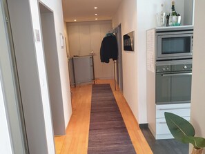 Een moderne keuken met een inbouwoven en magnetron, een houten vloer, en een donker kleed dat naar een gang leidt.
