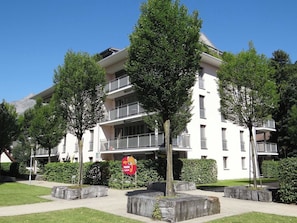 Een meerhoog gebouw met balkons, omgeven door bomen en stenen plantenbakken.