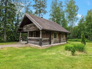 En rustik trästuga med ett sluttande tak, en veranda och en liten trädgård framför huset.