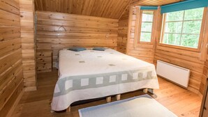 Un dormitorio de cabaña de madera con cama, ventana y radiador.