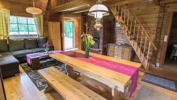 A wooden interior with a sofa, a dining table with benches, a fireplace, and a staircase.