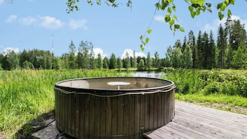 Een hottub op een houten terras, met een rivier en bos op de achtergrond.