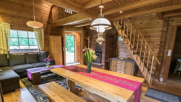 Un acogedor interior de cabaña con una mesa de comedor de madera, bancos, un sofá y una escalera.