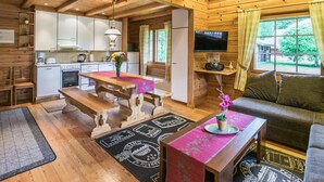 Un acogedor interior de cabaña con una mesa de comedor de madera, un sofá, un televisor y una zona de cocina.