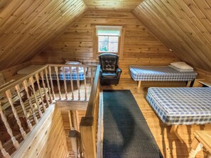 Ein Schlafzimmer im Loft-Stil mit Holzbalkendecke, einem schwarzen Lederstuhl, zwei Matratzen, einem kleinen Tisch und einem Fenster.