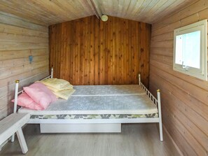 A single bed with a mattress and pillows, a small bedside table, and a window with blinds.