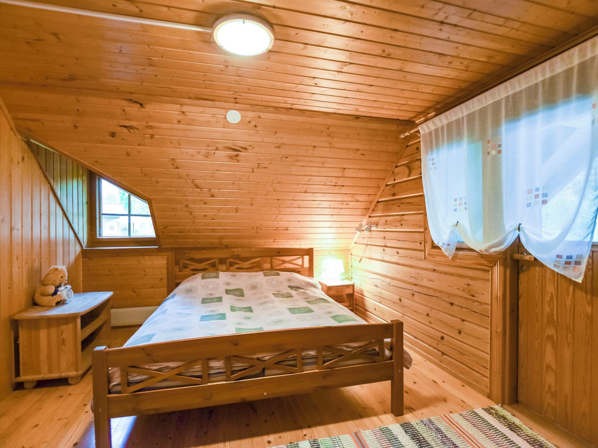 Une chambre à coucher dans un chalet en bois, avec un lit, une table de chevet, un ours en peluche et une fenêtre.