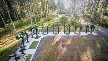 An outdoor gym area with exercise equipment, surrounded by a forest.