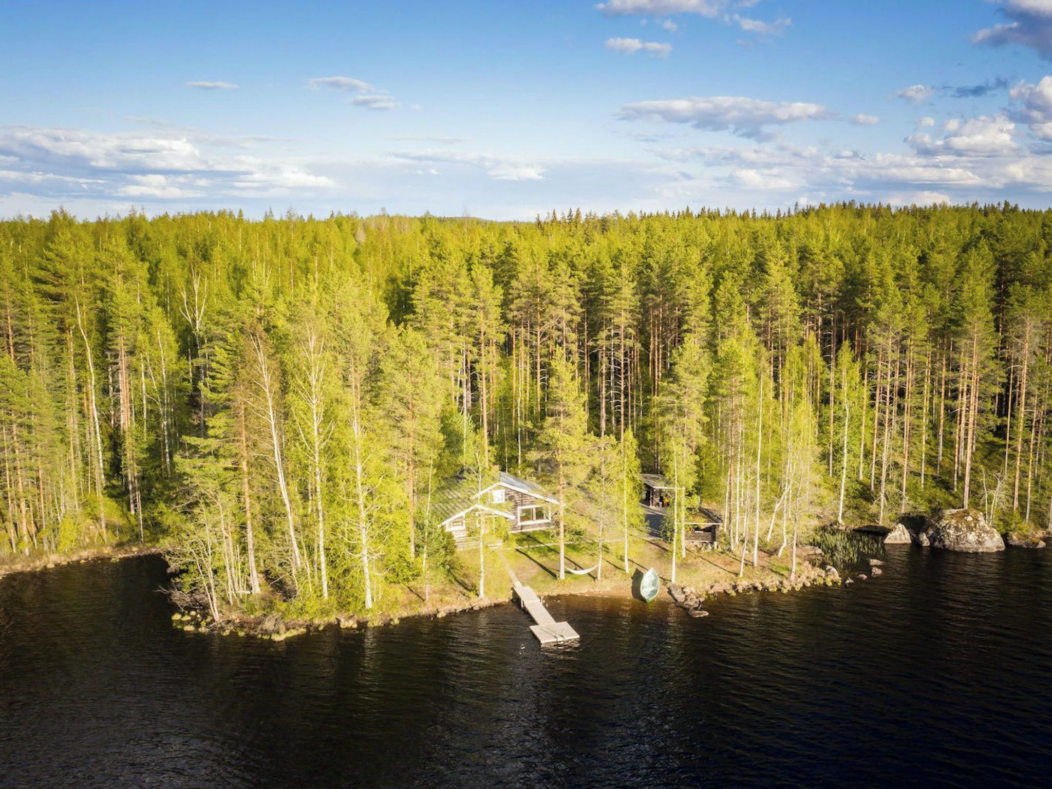 Une cabane avec un quai s’avançant dans un lac, entourée d’une forêt dense.
