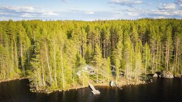 Une cabane avec un quai s’avançant dans un lac, entourée d’une forêt dense.