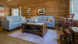 Ein gemütliches Blockhaus-Interieur mit zwei Sofas, einem Couchtisch, einem Holzstuhl und einer Stehlampe.
