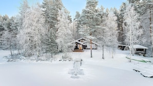 Eine Hütte, umgeben von schneebedeckten Bäumen, unter blauem Himmel.