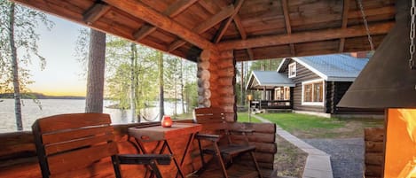 A wooden deck with seating, overlooking a lake and a cabin.