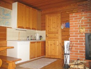 L’intérieur d’une cabane en bois comprend un espace cuisine avec des meubles de rangement en bois, un plan de travail blanc et un mur en briques.