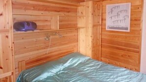 A wooden cabin room with a bed, a shelf with a speaker, and a poster on the wall. - Takaharju by Interhome (Posio)