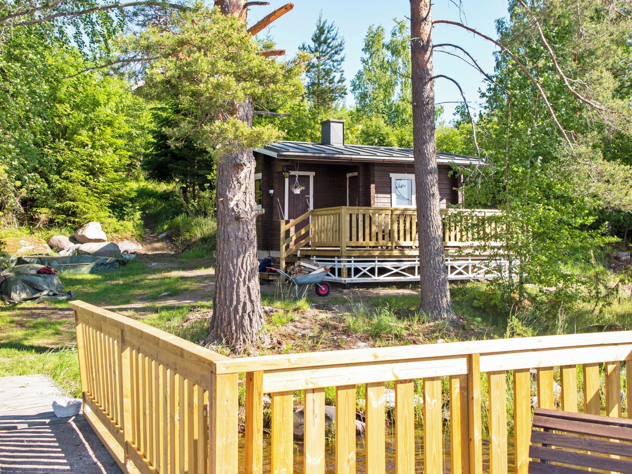 A cabin with a deck, surrounded by trees and a wooden fence.