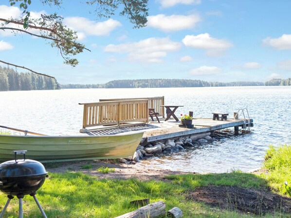 A lakeside dock with a boat, a grill, and a wooden deck with seating.