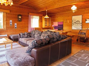 A cozy log cabin interior with a leather sofa, wooden walls, a dining table, and a kitchen area.