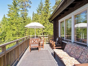 Une terrasse en bois aménagée avec du mobilier d’extérieur, notamment un canapé et des fauteuils, ainsi qu’un grand parasol.