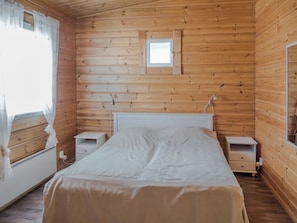 A wooden cabin bedroom with a single bed, two bedside tables, a small window, and a mirror.