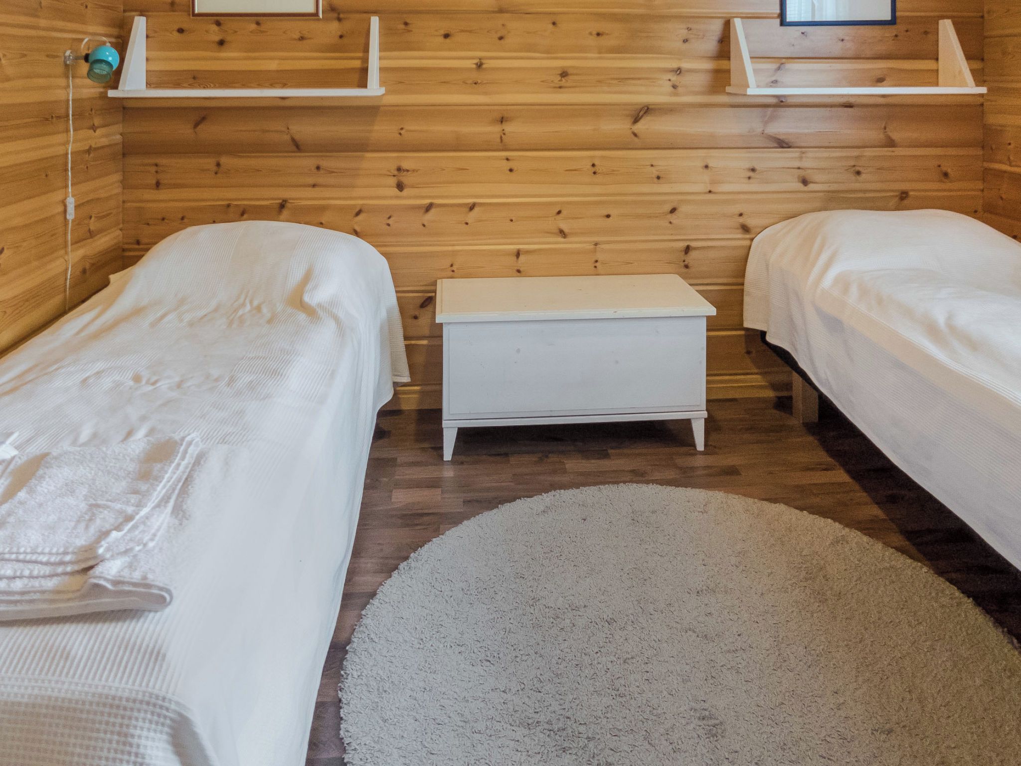 Une chambre avec deux lits simples, un petit banc blanc, des murs en bois et un tapis rond sur le sol.
