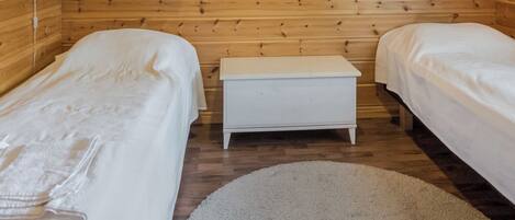 Ein Zimmer mit zwei Einzelbetten, einer kleinen weißen Bank, Holzwänden und einem runden Teppich auf dem Boden.