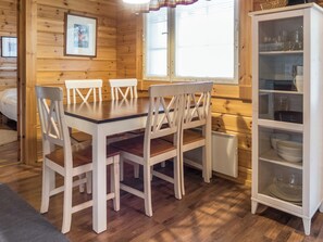 Ein Holzinterieur mit einem Esstisch und Stühlen, einem Küchenschrank mit Geschirr und einem gerahmten Bild an der Wand.