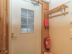Une porte en bois avec une fenêtre, un extincteur fixé au mur et une étagère en bois avec des crochets.