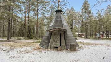 A conical wooden structure with a door, surrounded by a forest with tall trees.
